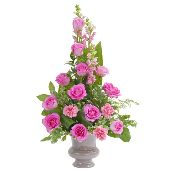 Tall arrangement of pink roses, carnations, and snapdragons in a gray urn-style vase