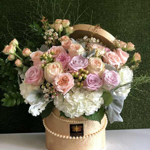 Round hatbox arrangement of pastel roses and white hydrangeas accented with pearls and filler blooms.