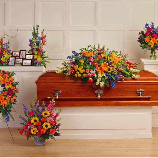 Colorful sympathy flowers with casket spray, standing sprays, wreaths, and vase around a wood casket