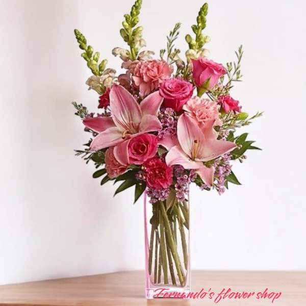 Tall pink arrangement with lilies, roses, and carnations in a clear rectangular glass vase
