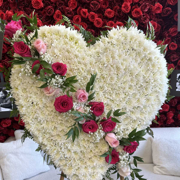 Heart-shaped white floral arrangement with pink roses on an easel