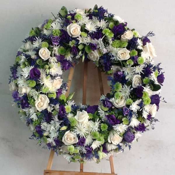 Round floral wreath with white, purple, and green flowers on an easel