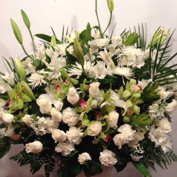 Large white floral arrangement with lilies, roses, and orchids in a pale vase