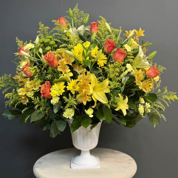 Yellow and coral mixed flower arrangement in a white pedestal vase