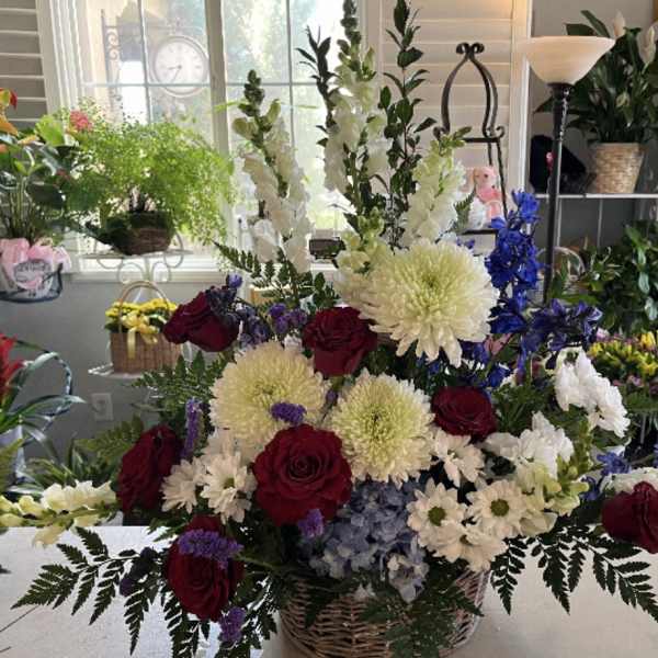 Large mixed flower arrangement in a wicker basket with red roses and white blooms