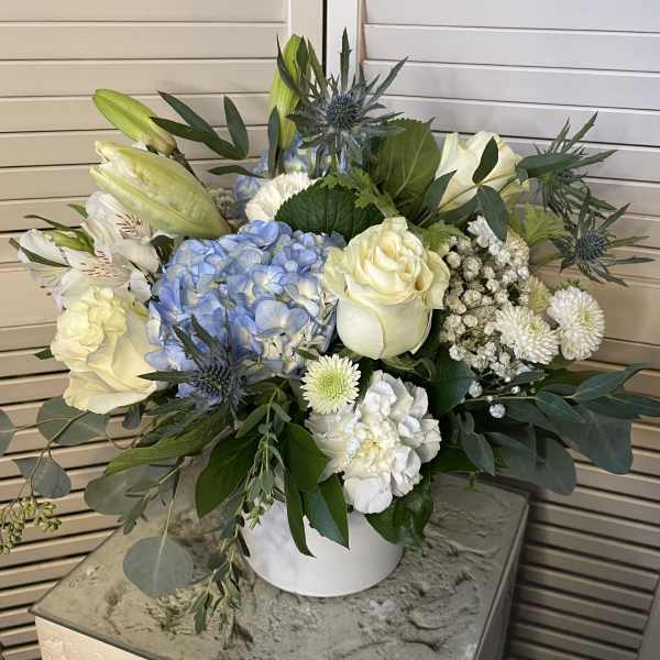 White roses and blue hydrangeas in a white vase with mixed greenery