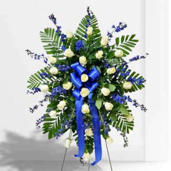 Standing floral spray with white roses, blue flowers, and a blue ribbon