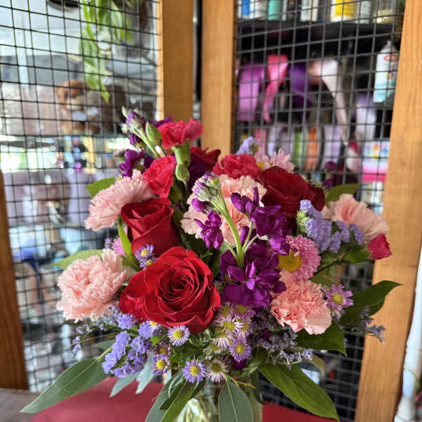 Mixed bouquet of red roses, pink carnations, and purple flowers in a glass vase