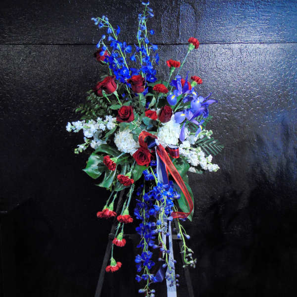 Standing spray of red roses and carnations with blue delphinium and white flowers on an easel