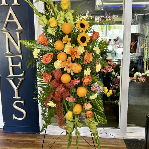 Tall floral standing spray with oranges, sunflowers, and peach roses