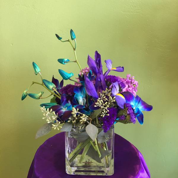 Purple and blue floral arrangement in a clear square vase