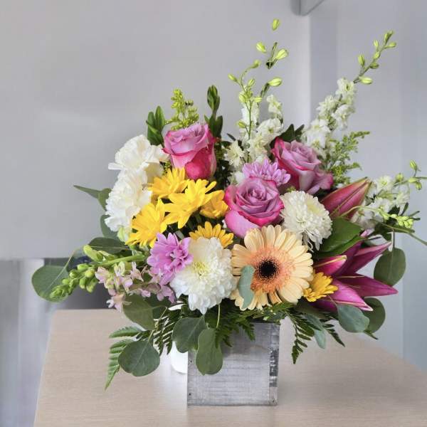 Mixed bouquet with pink roses, yellow daisies, and white blooms in a square vase