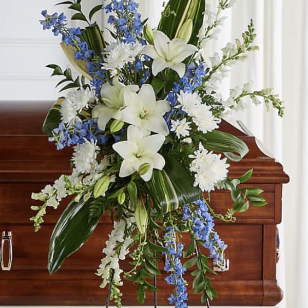 White lilies and blue flowers arranged on a wooden casket