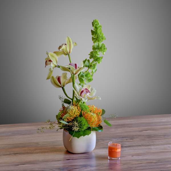 Tall floral arrangement in a white vase with orange and green blooms