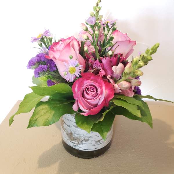 Pink roses and purple flowers arranged in a small vase