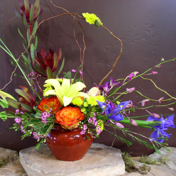 Colorful floral arrangement in a red vase with lilies, roses, and orchids