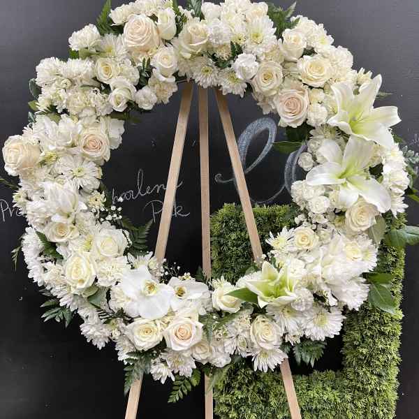 White floral wreath on a wooden easel with roses and lilies