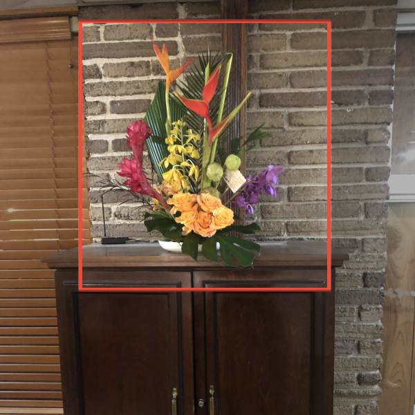 Tropical flower arrangement with orange heliconia and orchids in a white vase