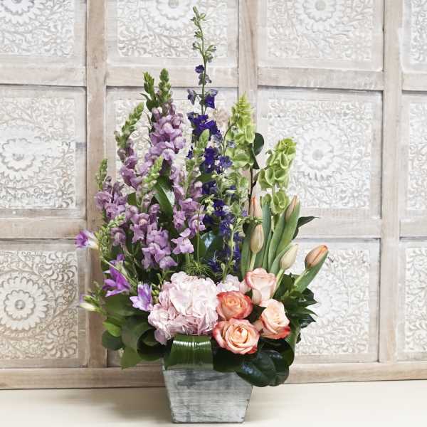 Tall mixed bouquet with roses, tulips, and purple spikes in a gray vase