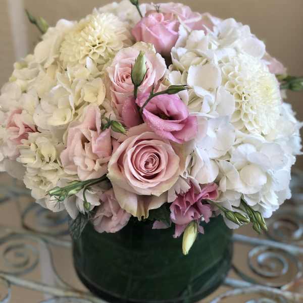 Low round arrangement of white hydrangeas, white dahlias, and pink roses in a green glass vase