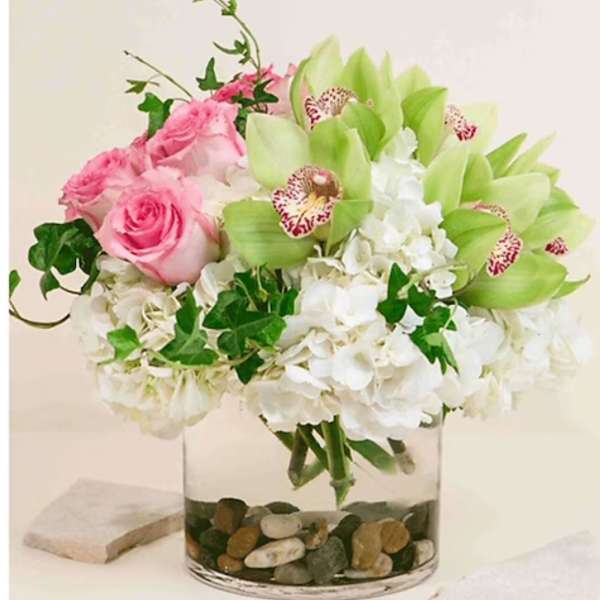 Pink roses and white hydrangeas in a clear glass vase with green orchids