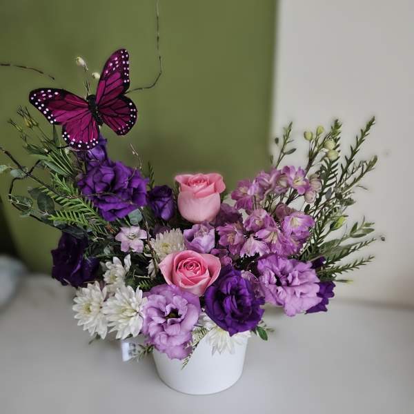 Purple and pink flower arrangement in a white pot with a butterfly pick