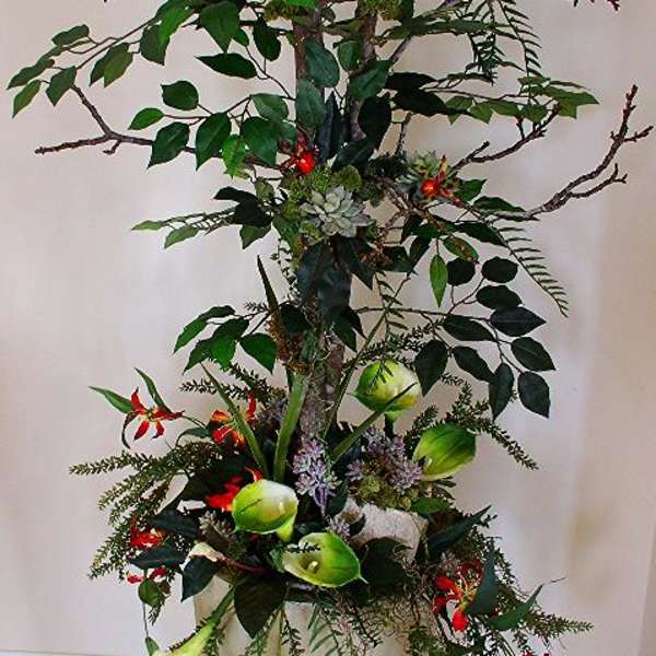 Tall floral arrangement with branches, red blooms, and green calla lilies in a white vase