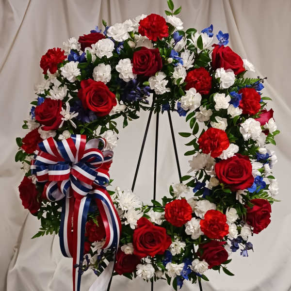 Circular wreath of red, white, and blue flowers on a stand with a ribbon bow