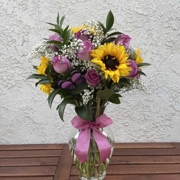 Bouquet of pink roses and yellow sunflowers in a glass vase with a pink ribbon