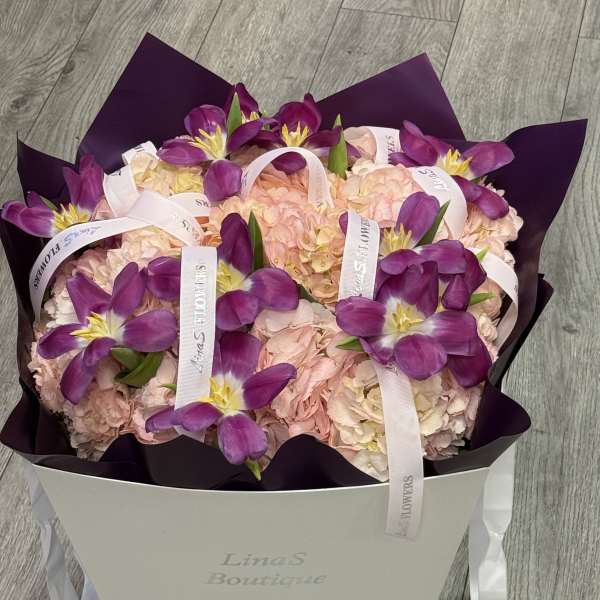 Purple tulips arranged over pale pink hydrangeas in a white box