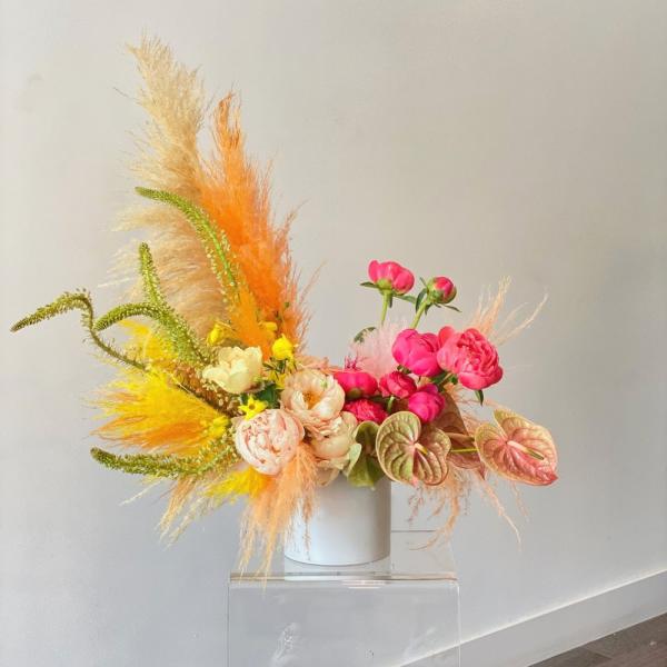 Bright floral arrangement with pink blooms and orange feathery accents in a white vase