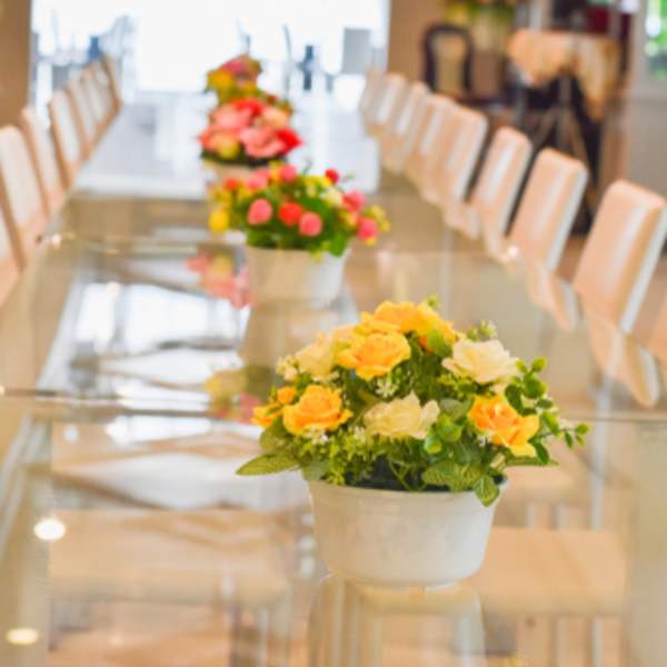 Flower centerpieces in white pots on a long table with white chairs
