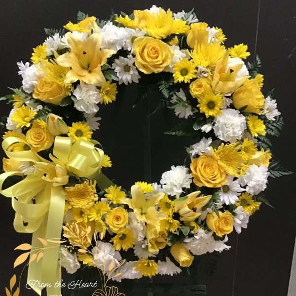 Yellow and white floral wreath with a ribbon bow on a dark stand