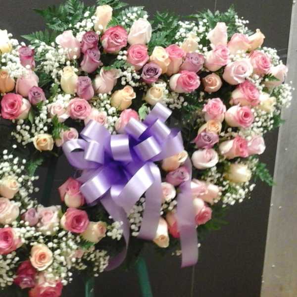 Heart-shaped wreath of pink and cream roses with a purple bow
