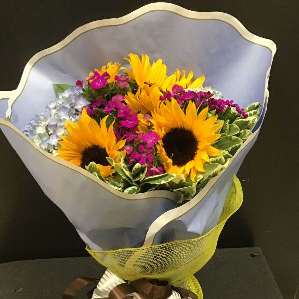 Bouquet of sunflowers and small purple flowers wrapped in pale paper