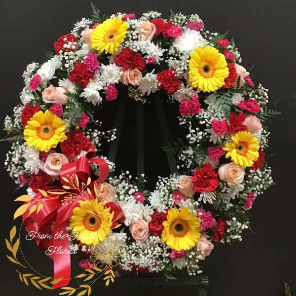 Circular floral wreath with yellow gerbera daisies, pink roses, and red carnations