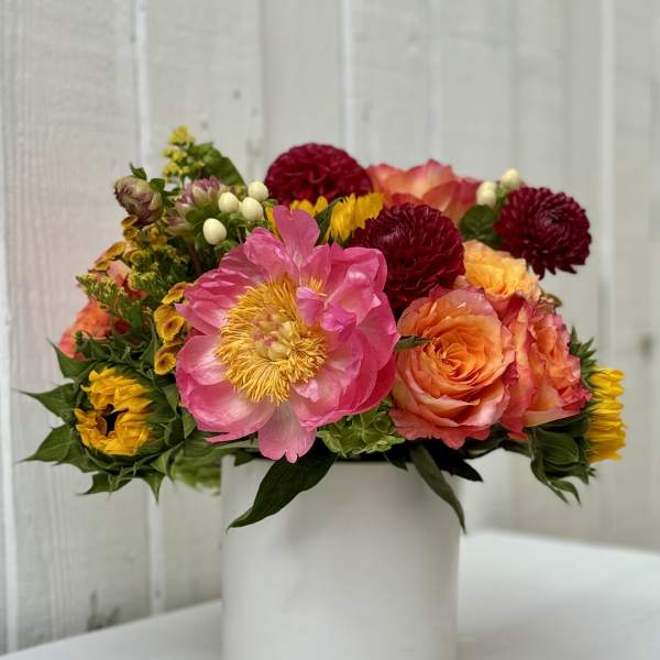 Bright arrangement of pink peony, orange roses, and yellow blooms in a white cylinder vase