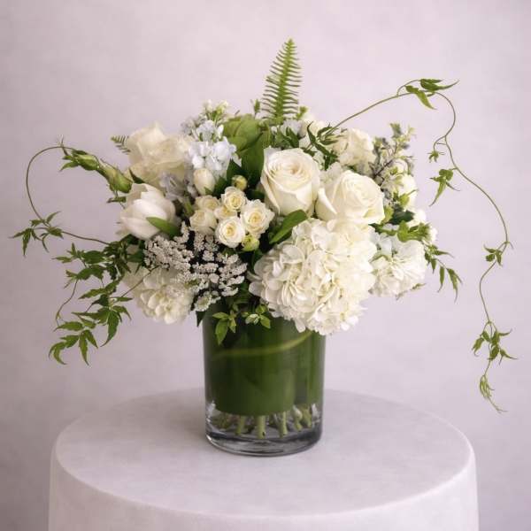 White floral arrangement in a glass vase with trailing greenery