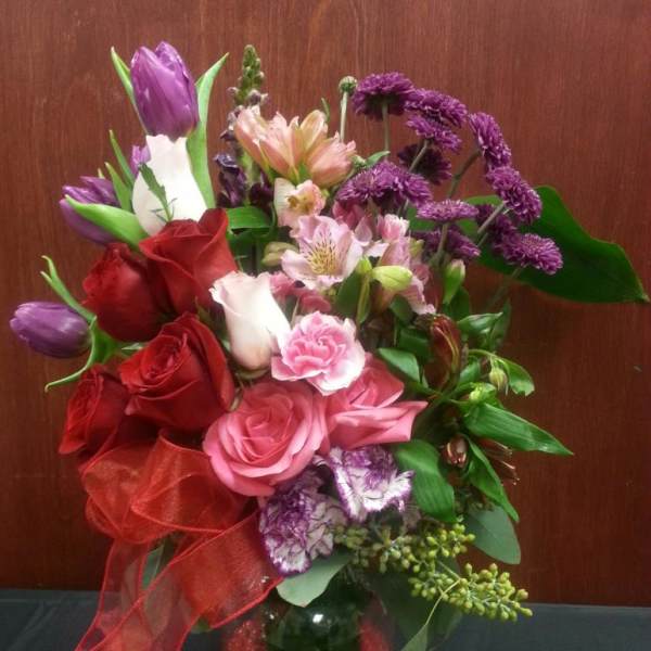 Bouquet of roses, tulips, and purple flowers in a pink glass vase