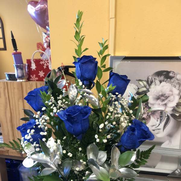 Blue roses arranged with baby's breath and greenery in a vase.