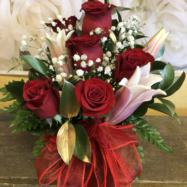 Red roses and pink lilies arranged with baby's breath in a red ribbon wrap