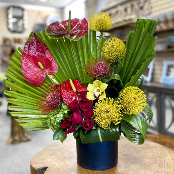 Tropical bouquet with red anthuriums, yellow blooms, and roses in a black vase