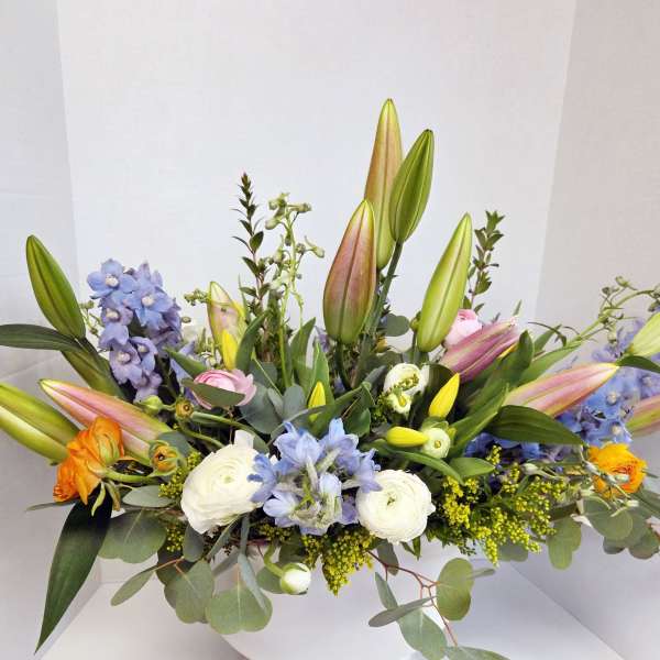 Mixed bouquet with lilies, blue flowers, and white blooms in a white vase