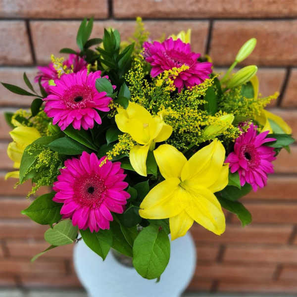 Bouquet of pink gerbera daisies and yellow lilies in a white vase