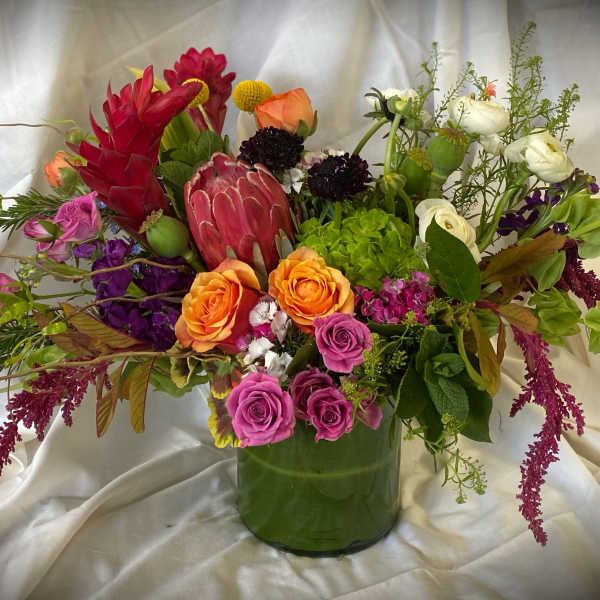 Mixed bouquet in a green glass vase with orange, pink, purple, and white blooms