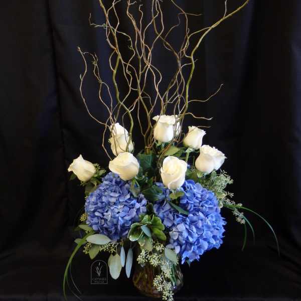 White roses and blue hydrangeas in a glass vase with curly branches
