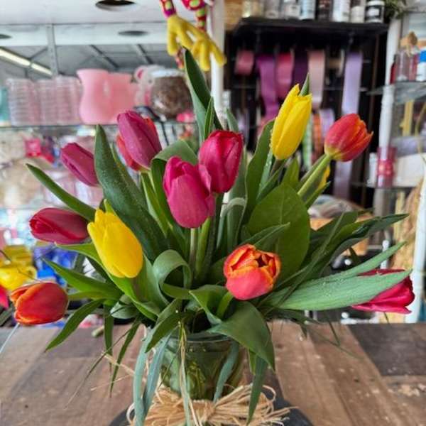 Colorful tulips arranged in a glass vase with a raffia bow