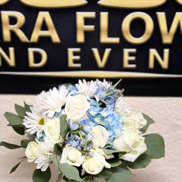 Bouquet of white roses, blue hydrangeas, and white daisies in a glass vase