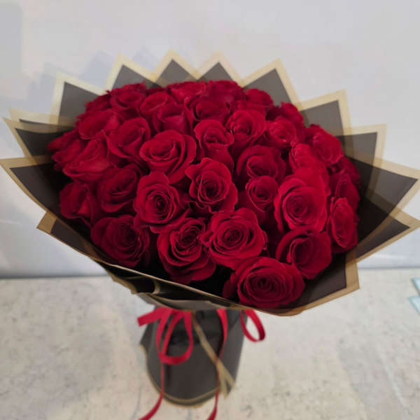 Bouquet of red roses wrapped in black and gold paper with a red ribbon