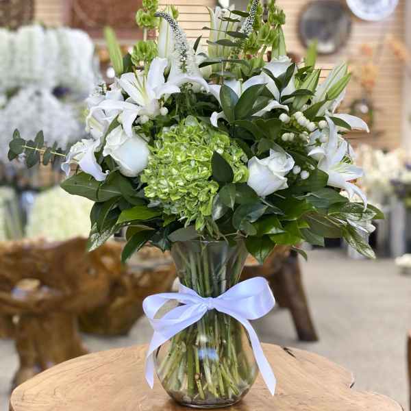 White lilies and roses in a glass vase with a blue ribbon